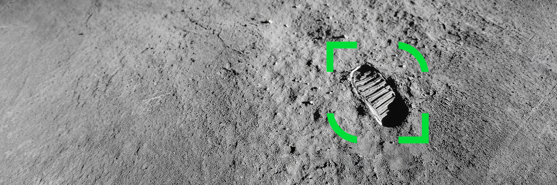 Fotspår på en sandig, grå yta markerat med en grön rektangel i mitten av bilden.